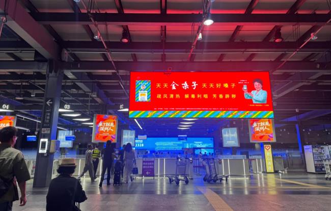 深圳机场出租车等候区大屏红底广告吸睛，旅客步履匆匆过 