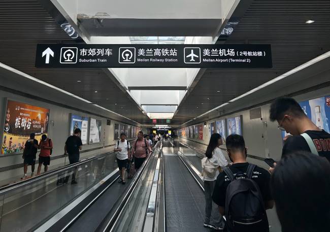 美兰高铁站换乘通道中间有扶梯步道，两侧有当地文旅相关灯箱广告