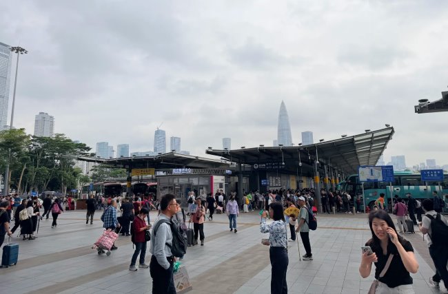深圳湾口岸入口处日景实拍图，出入境连廊两侧停靠着过港大巴车，背后有深圳湾地标建筑春笋入镜