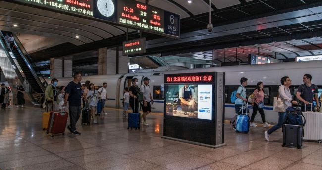 图为北京南站站台层，拿着行李箱的旅客穿梭在列车与扶梯之间
