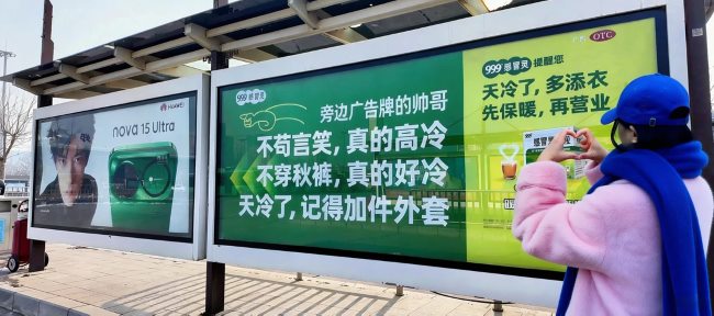 图为2026年1月期间美团买药创意候车亭广告，联动隔壁候车亭广告挂牌的帅哥代言人“加件衣服”