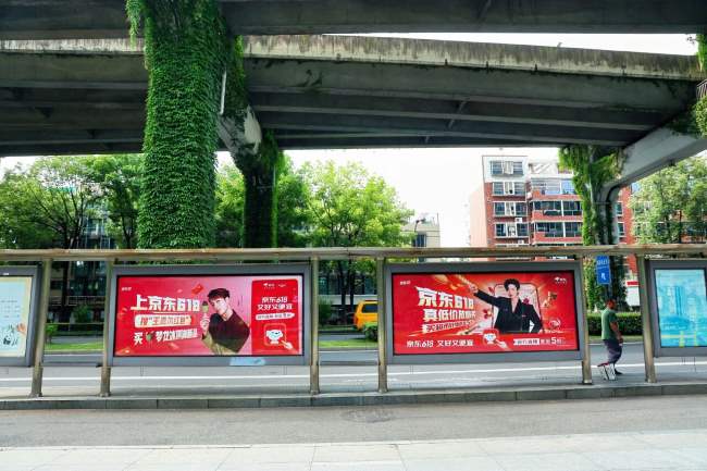 图为618期间京东在成都发布的公交候车亭广告，相邻两块的代言人画报分别是刘宇宁和王嘉尔