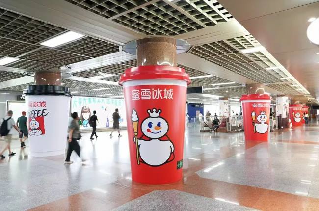 图为2026年9月蜜雪冰城在广州地铁站发布创意包柱咖啡杯广告实拍图，吸引乘客侧目